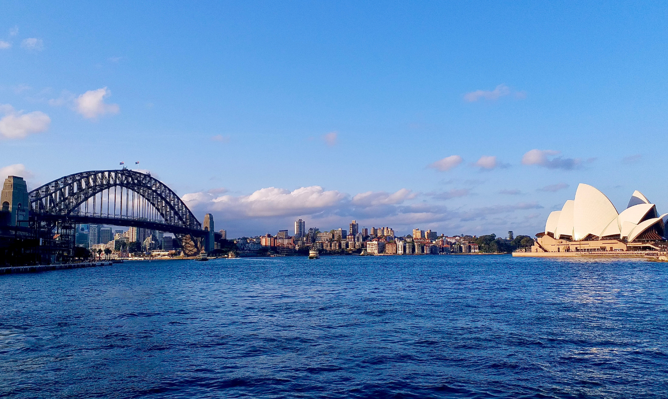 A picture of the sydney, australian skyline with water in the middle, the opera on the right and a bridge on the left